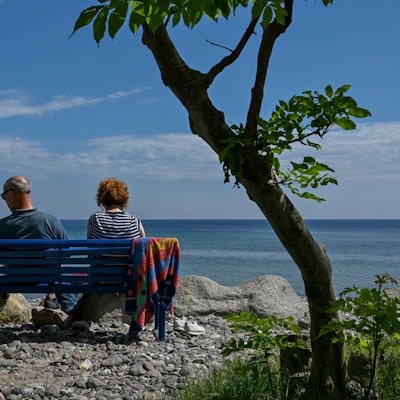 Ein Paar sitzt auf einer blauen Bank am Meer.