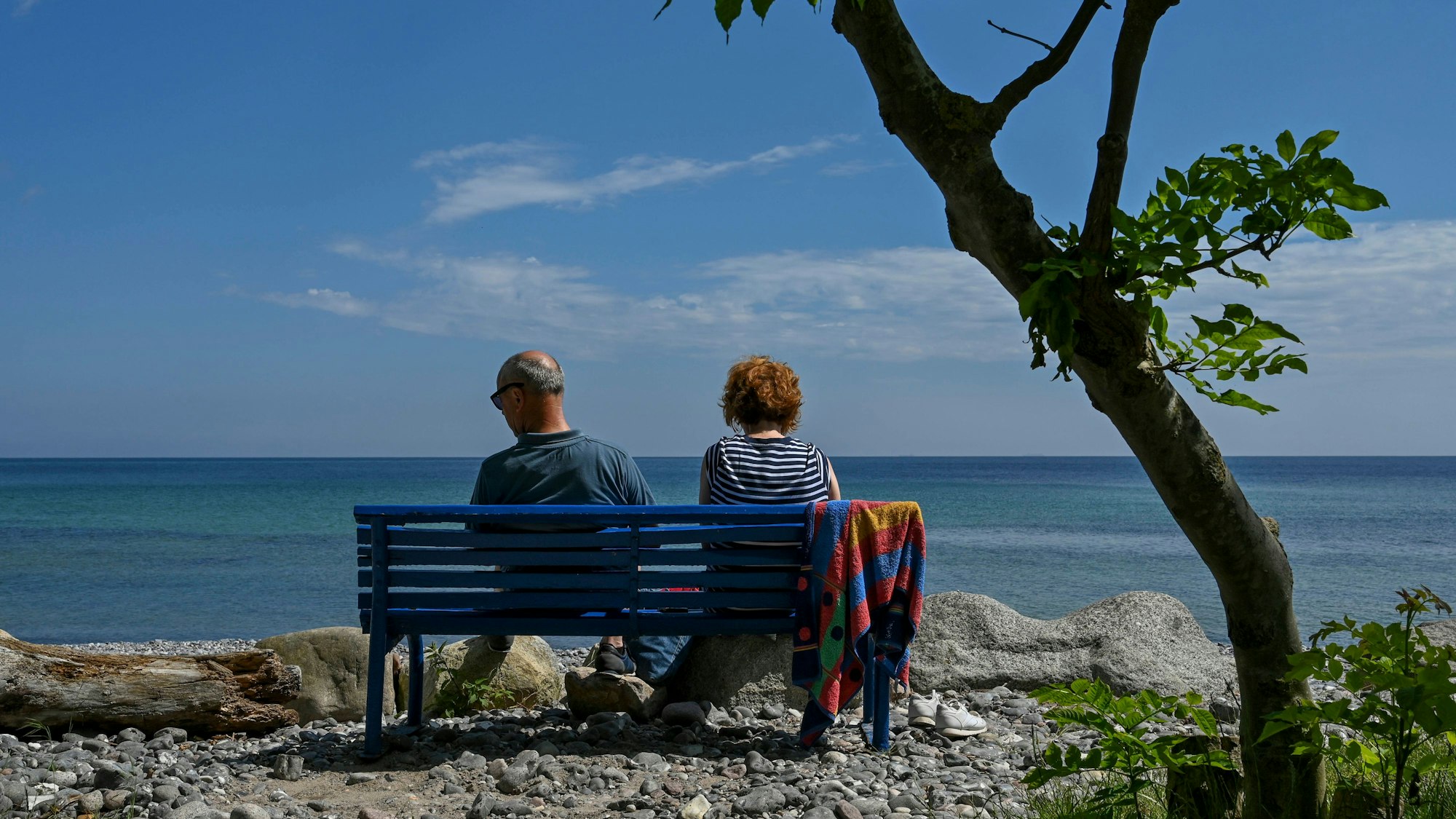 Ein Paar sitzt auf einer blauen Bank am Meer.