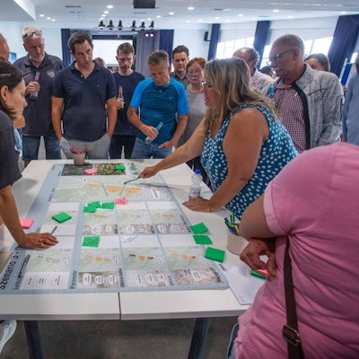 Menschen beugen sich über auf einem Tisch ausgebreitete Pläne.