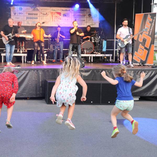 Drei Kinder hüpfen vor der Bühne des Open-Air-Konzerts zum Feuerwehrjubiläum in Wiehl Marienhagen.
