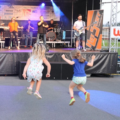Drei Kinder hüpfen vor der Bühne des Open-Air-Konzerts zum Feuerwehrjubiläum in Wiehl Marienhagen.