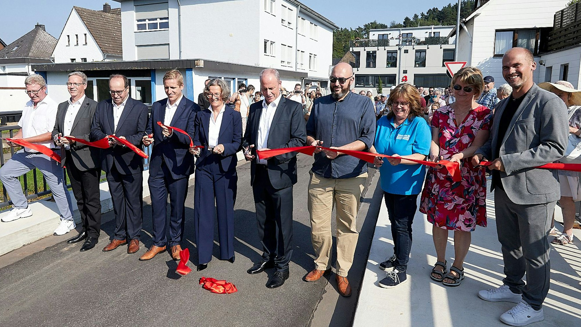 Die Brücke über die Urft in den Weiherbenden wird wiedereröffnet, in dem ein Band durchschnitten wird. Zehn Personen stehen direkt an dem roten Band.