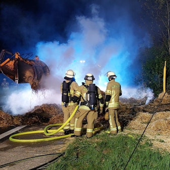 Helfer der Feuerwehr löschen Strohballen auf einer Wiese.