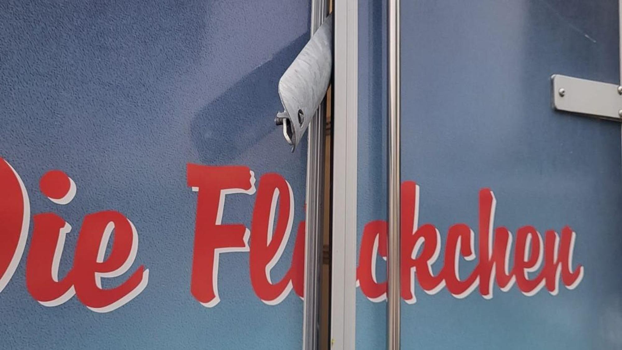 Im Türspalt eines Pkw-Anhängers mi der Aufschrift „Die Flöckchen“ steckt die Metallabdeckung einer Laternenstromzuführung.