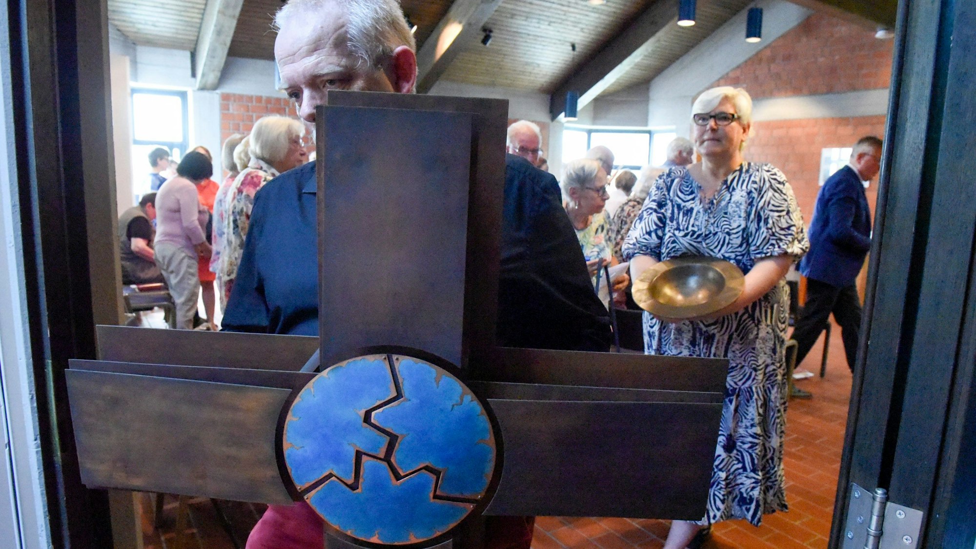 Zu sehen ist ein Mann, der ein Kreuz aus dem Gebäude trägt.