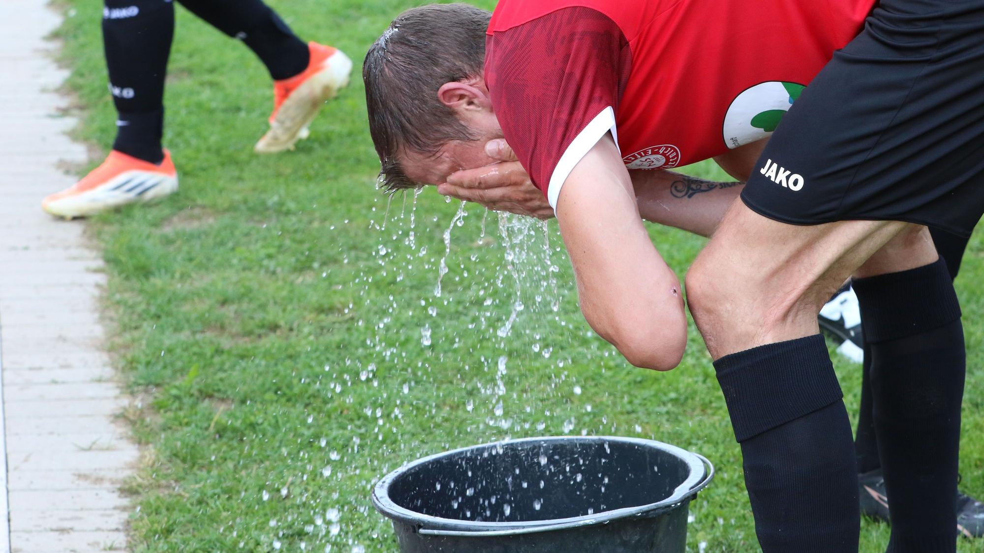 Ein Fußballer kühlt sich mit Wasser aus einem Eimer.