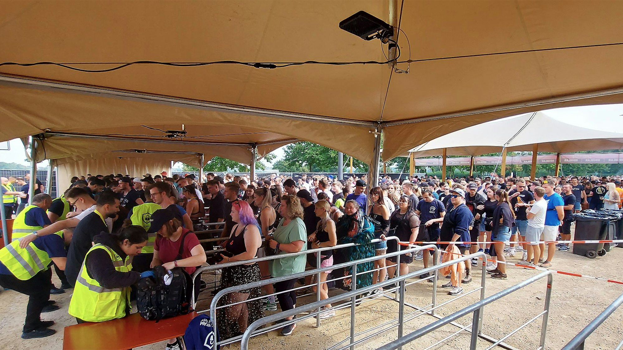 Das Bild zeigt die Kontrollen am Eingang. Es haben sich lange Schlangen gebildet, weil die Taschen gründlich kontrolliert werden.