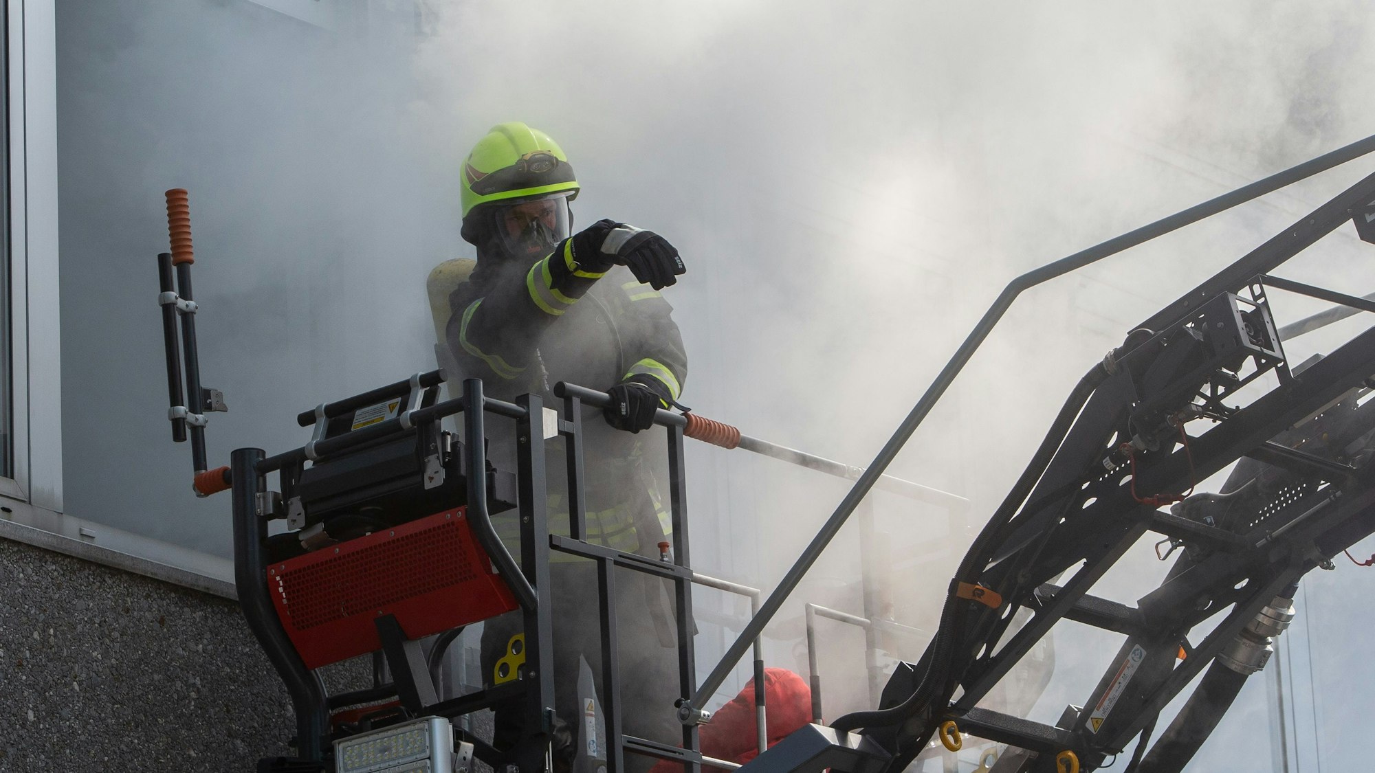 Ein Feuerwehrmann steht mit Atemschutzausrüstung im Korb einer Drehleiter.