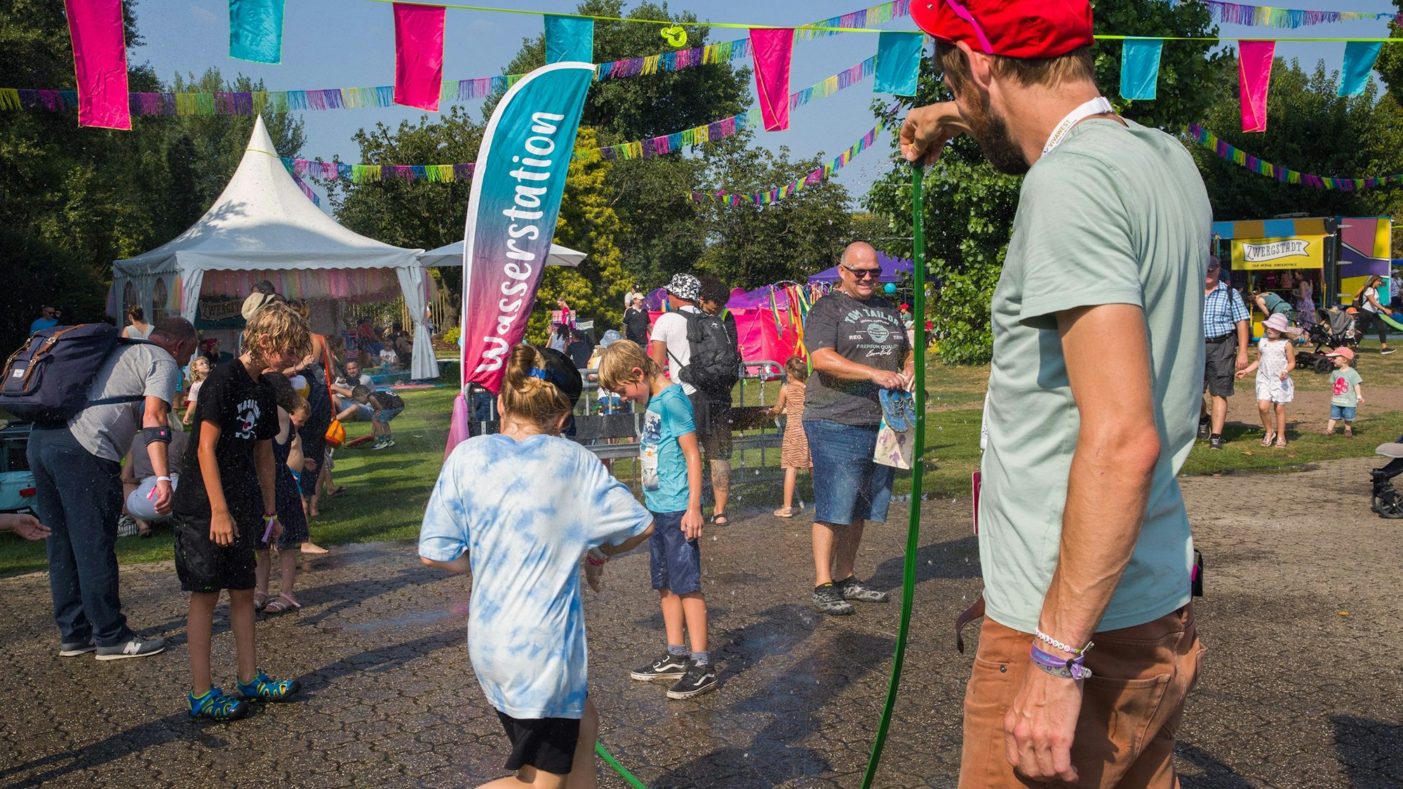 Kinder laufen durch den Wasserstrahl eines Gartenschlauchs und kühlen sich ab.