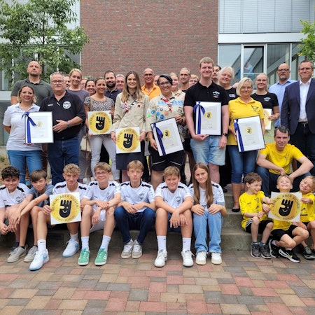 Kinder und Erwachsene halten eine Auszeichnung in den Händen.