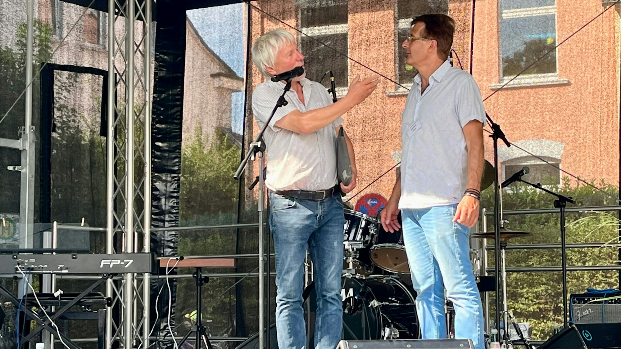 Zwei Männer stehen auf einer Bühne und sprechen miteinander.