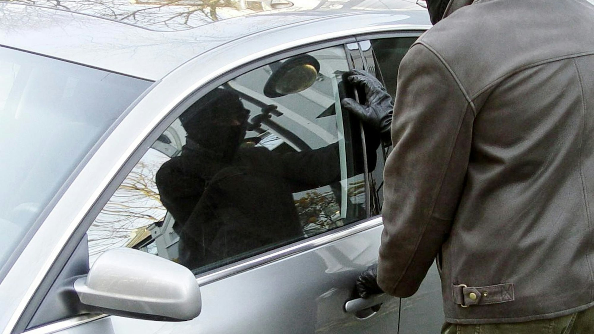 Ein maskierter Mann steht vor einer Autotür und versucht, diese zu öffnen.