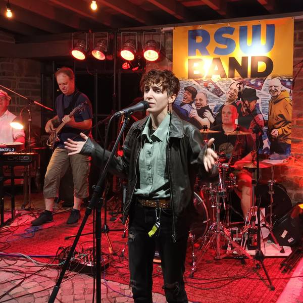 Eine Person singt am Mikrofon, umringt von Musikern