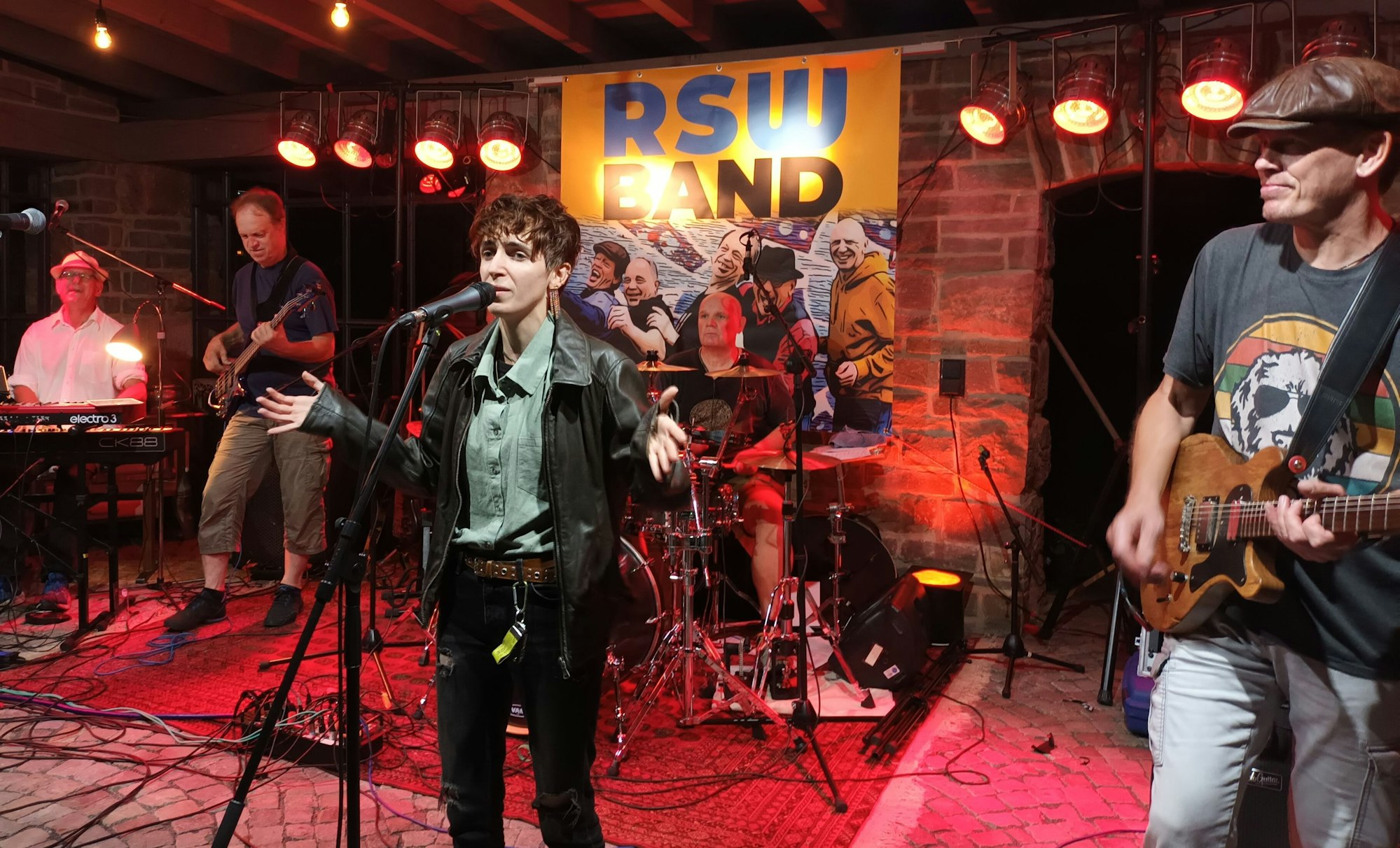 Eine Person singt am Mikrofon, umringt von Musikern
