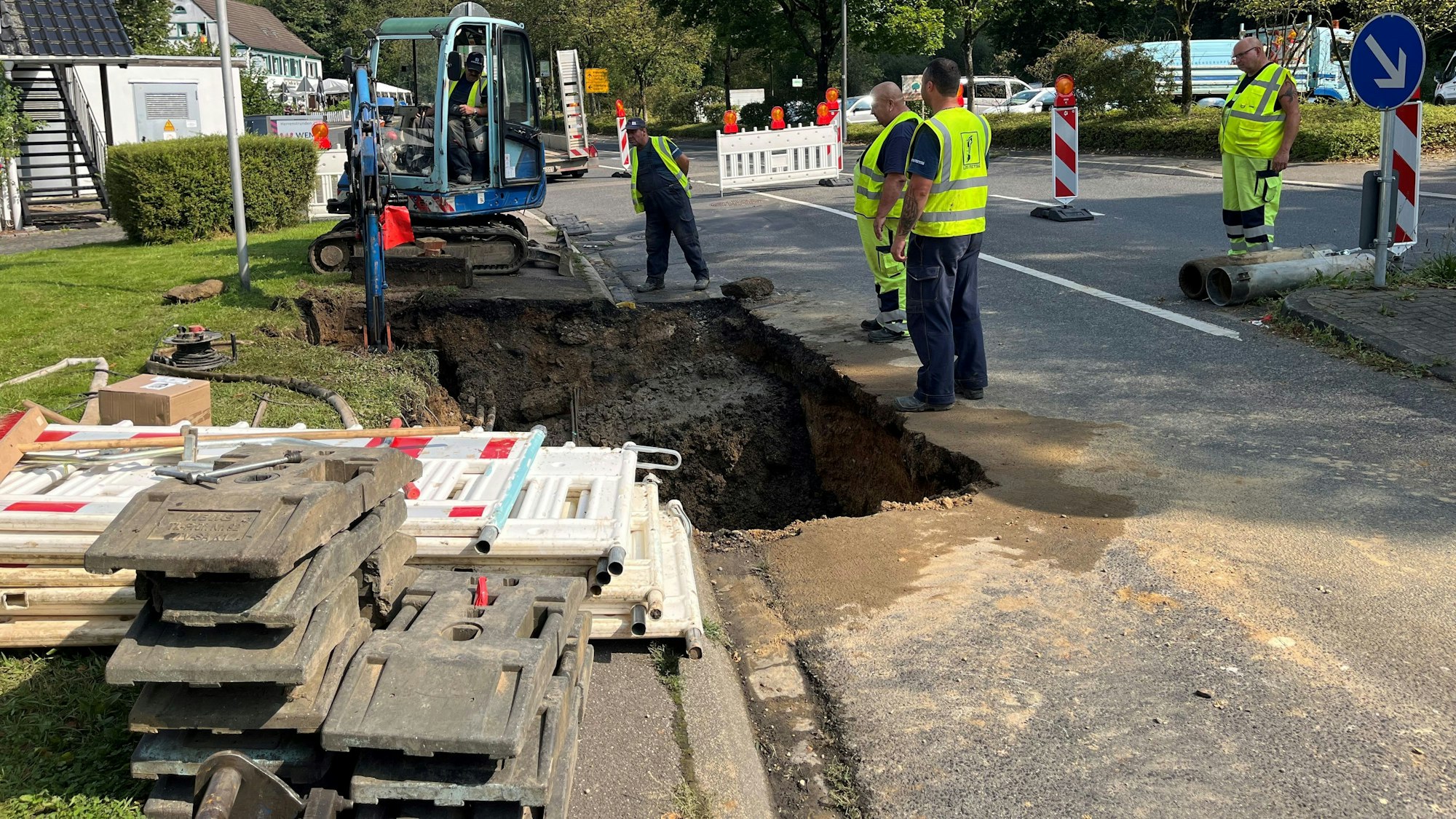 Um die Baugrube mit Bagger stehen die Arbeiter mit gelber Weste und begutachten die Leitungen im Untergrund.