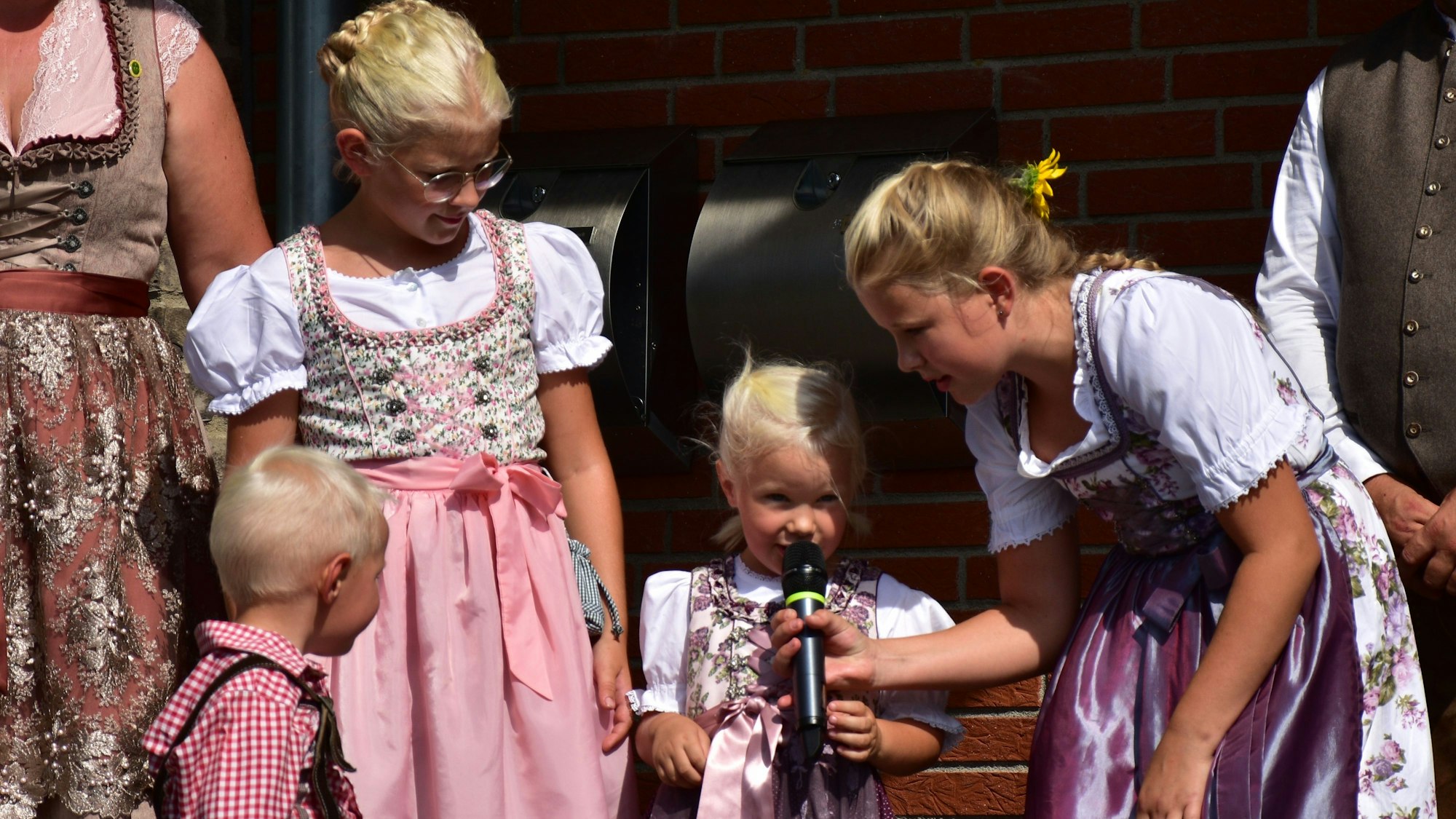 Drei blonde Mädchen mit Zopffrisuren und Dirndl am Mikrofon.