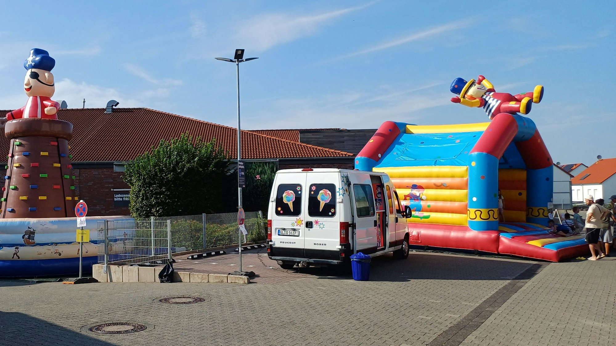 Zwei Erwachsene stehen auf einem leeren Platz vor einer Hüpfburg.