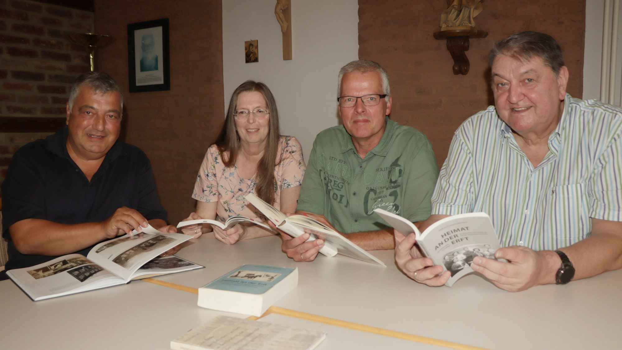Die Mitglieder des Rechercheteams sitzen an einem Tisch und halten jeweils ein Buch aufgeschlagen vor sich. Sie schauen in die Kamera. Auf dem Tisch liegt ein weiteres Buch.