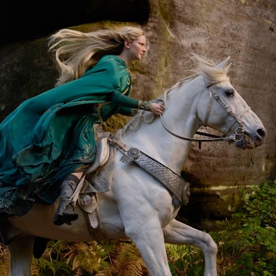 Die walisische Schauspielerin Morfydd Clark reitet in ihrer Rolle als Elbenkriegerin Galadriel in der Amazon-Prime-Video-Serie „Der Herr der Ringe: Die Ringe der Macht“ einen Schimmel. Ihre blonden Haare und ihre grünen Gewänder wehen im Wind.