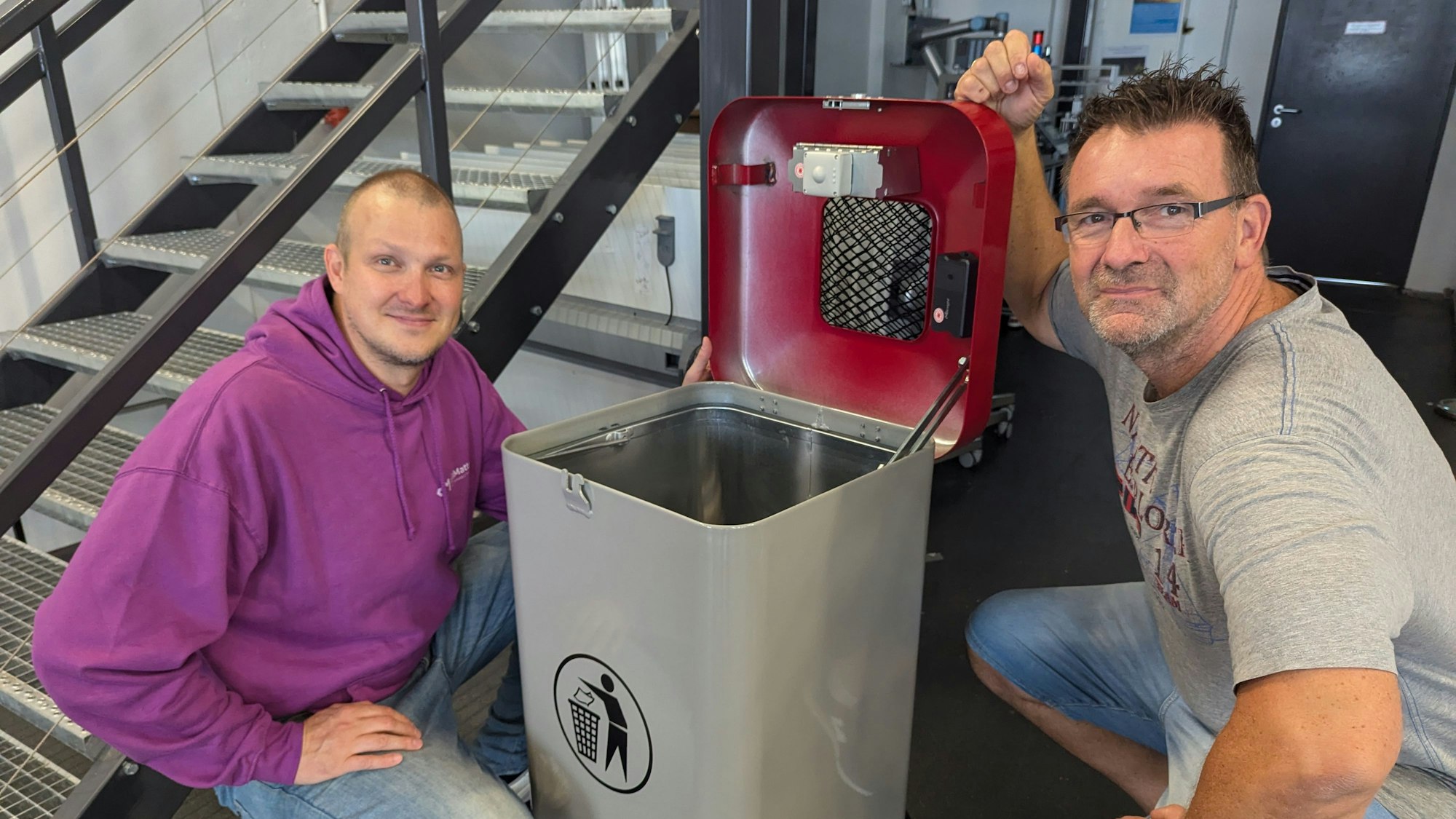 Zwei Männer hocken neben einem Mülleimer mit geöffnetem Deckel, in dem sich die Sensoren befinden.
