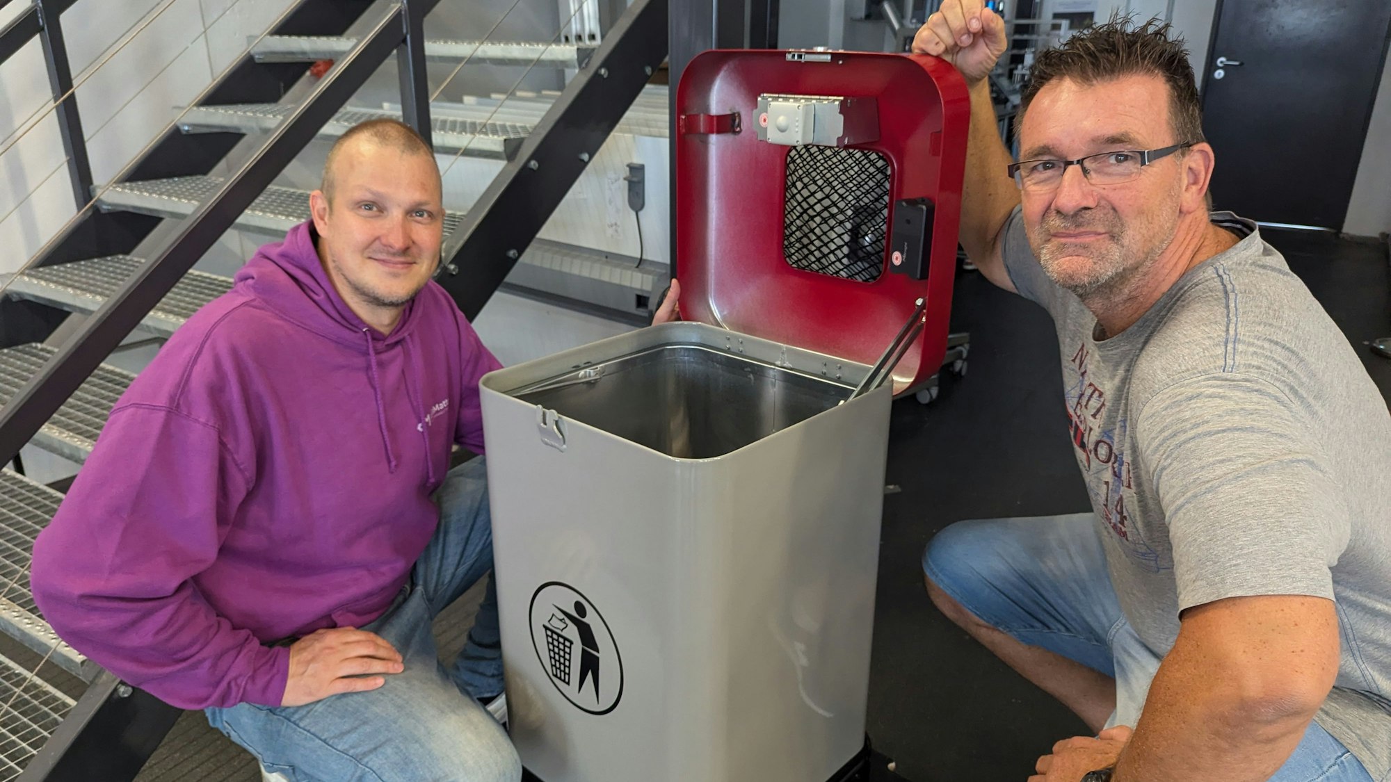 Das Foto zeigt zwei Männer, die neben einem Mülleimer hocken. Im geöffneten Deckel sind Sensoren zu erkennen.