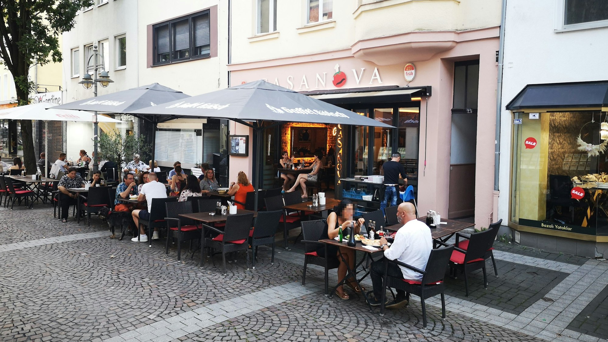 Der Außenbereich der Pizzeria Casanova in Brühl ist zu sehen. Es sitzen Menschen an Tischen und essen.