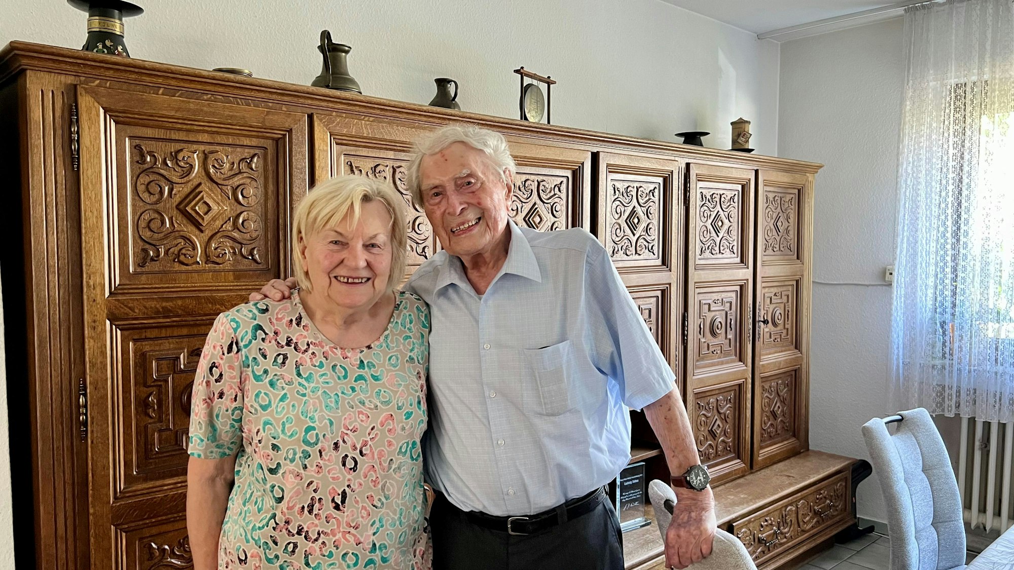 Ludwig Sebus und Inge Hellwig stehen vor einer Schrankwand im Wohnzimmer.