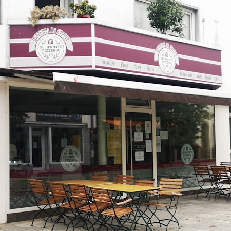 Die Pizzeria Selinunte Da Gianni in der Wesselinger Bahnhofstraße gehört zu den beliebtesten im Rhein-Erft-Kreis. Hier ist sie von außen zu sehen. Eine Jalousie ist eingefahren, draußen stehen Stühle und Tische.