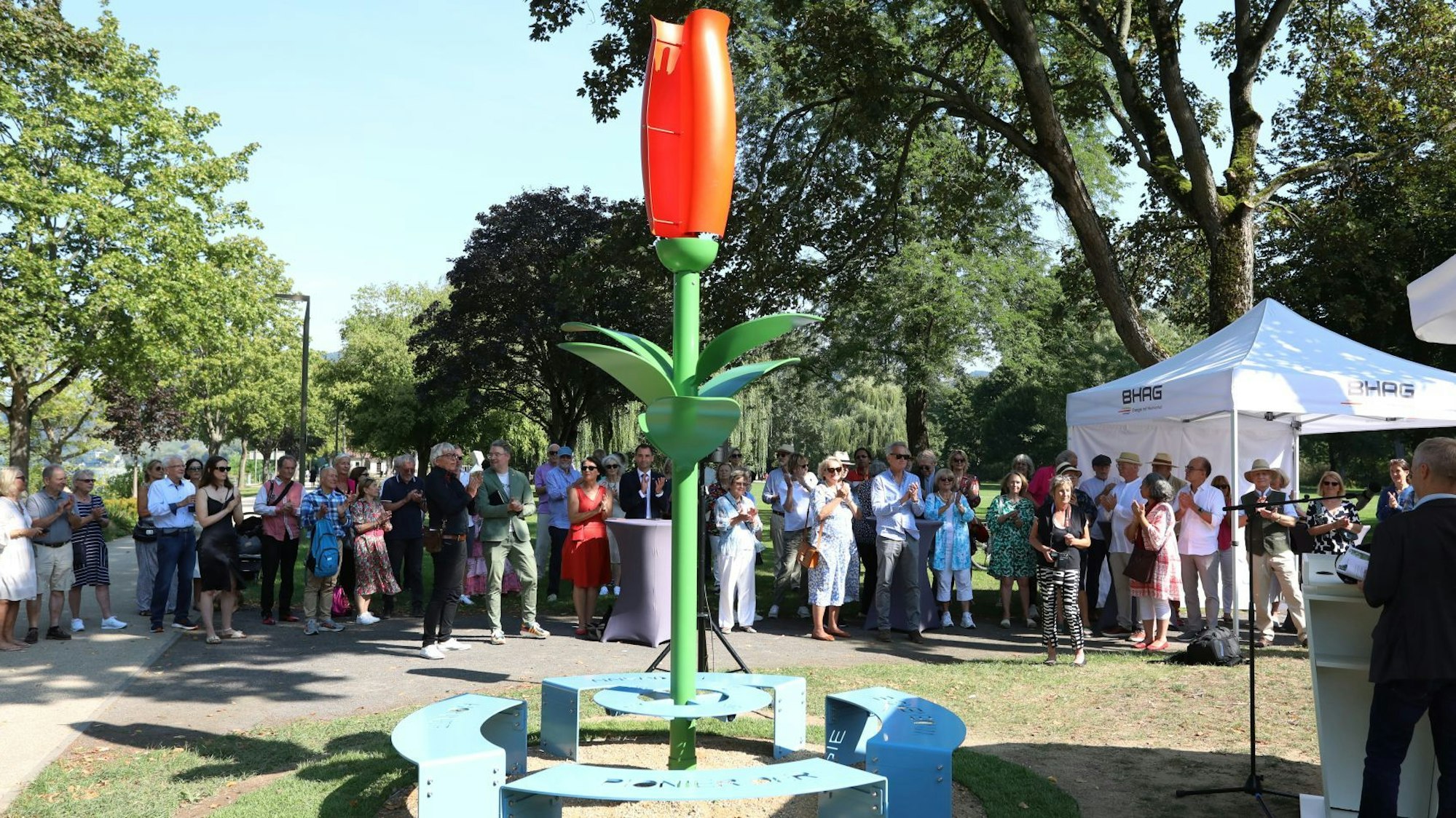 Eine Skulptur mit grünem Stiel und roter Blüte stellt ein Blume dar, im Hintergrund stehen viele Zuschauer.