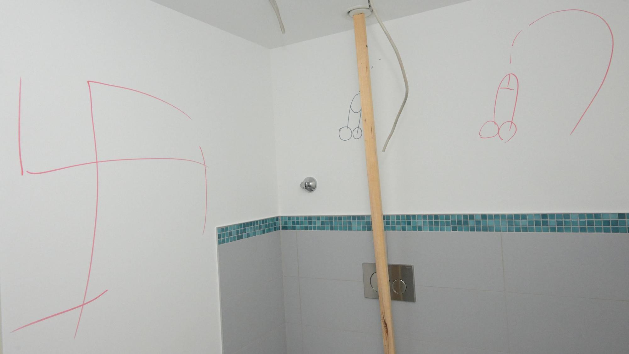 Hakenkreuze und Phallussymbole wurden an die weiße Wand einer Dusche geschmiert.