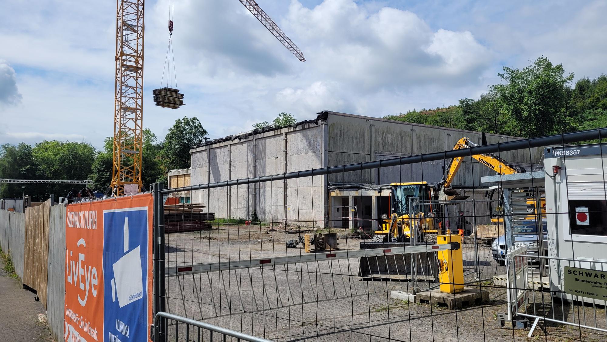Eine Halle aus Beton wird abgerissen. Kran und Bagger arbeiten.