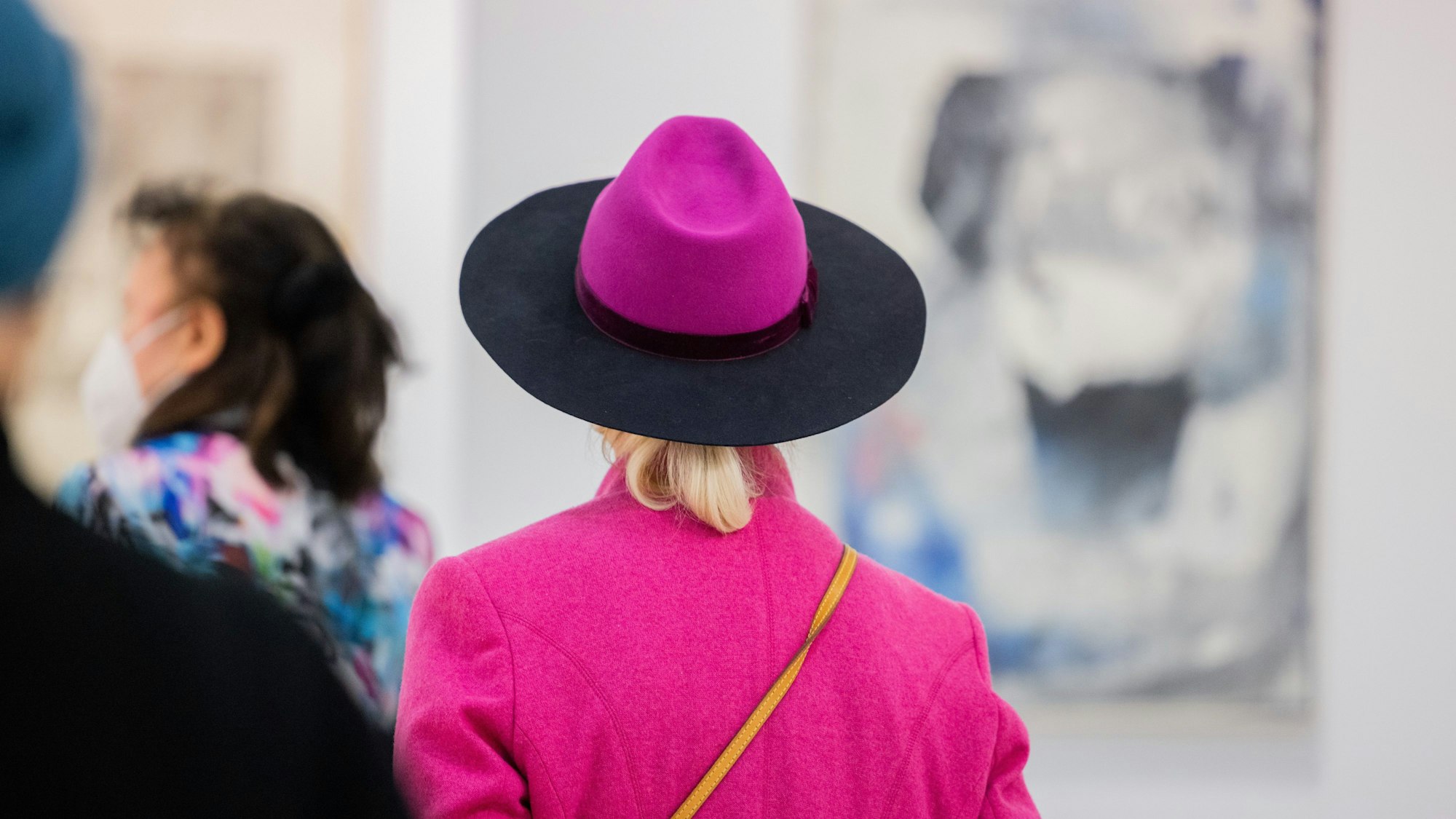 Eine Besucherin mit Hut geht über die Art Cologne.