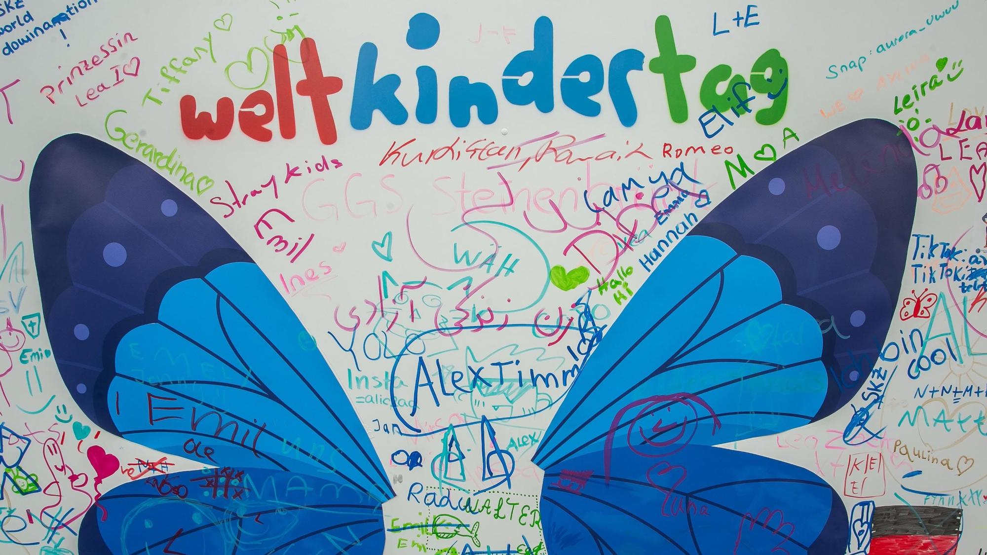 Ein Weltkindertag-Schriftzug zwischen einem aufgemalten Schmetterling.