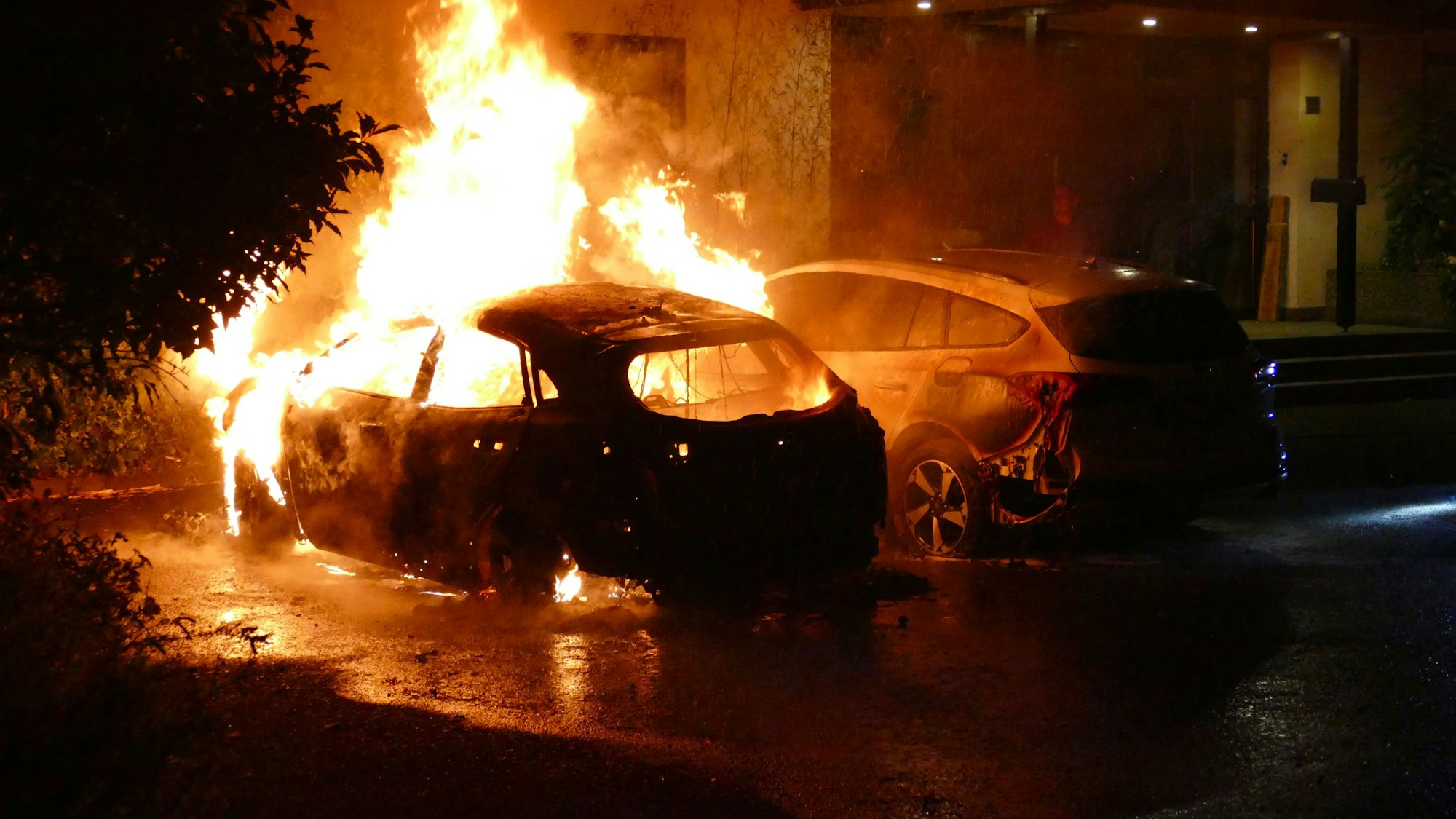 Zwei Autos brennen vor einem Haus.