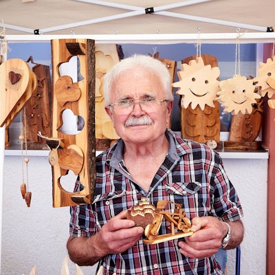 Peter Murges steht zwischen seinen Holzarbeiten, die er aufgehängt hat.