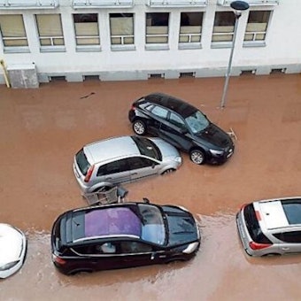 Die Straße ist überflutet. Autos stehen tief im braunen Wasser. Ein Wagen ist auf einen anderen geschoben worden.