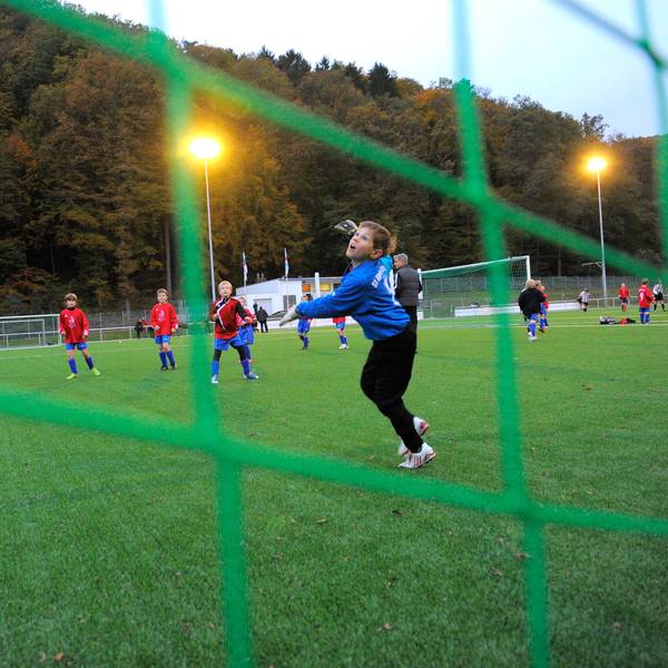 Blick durch das grüne Netz eines Fußballtores auf einen Jungen, der gerade einem Ball hinterherschaut.