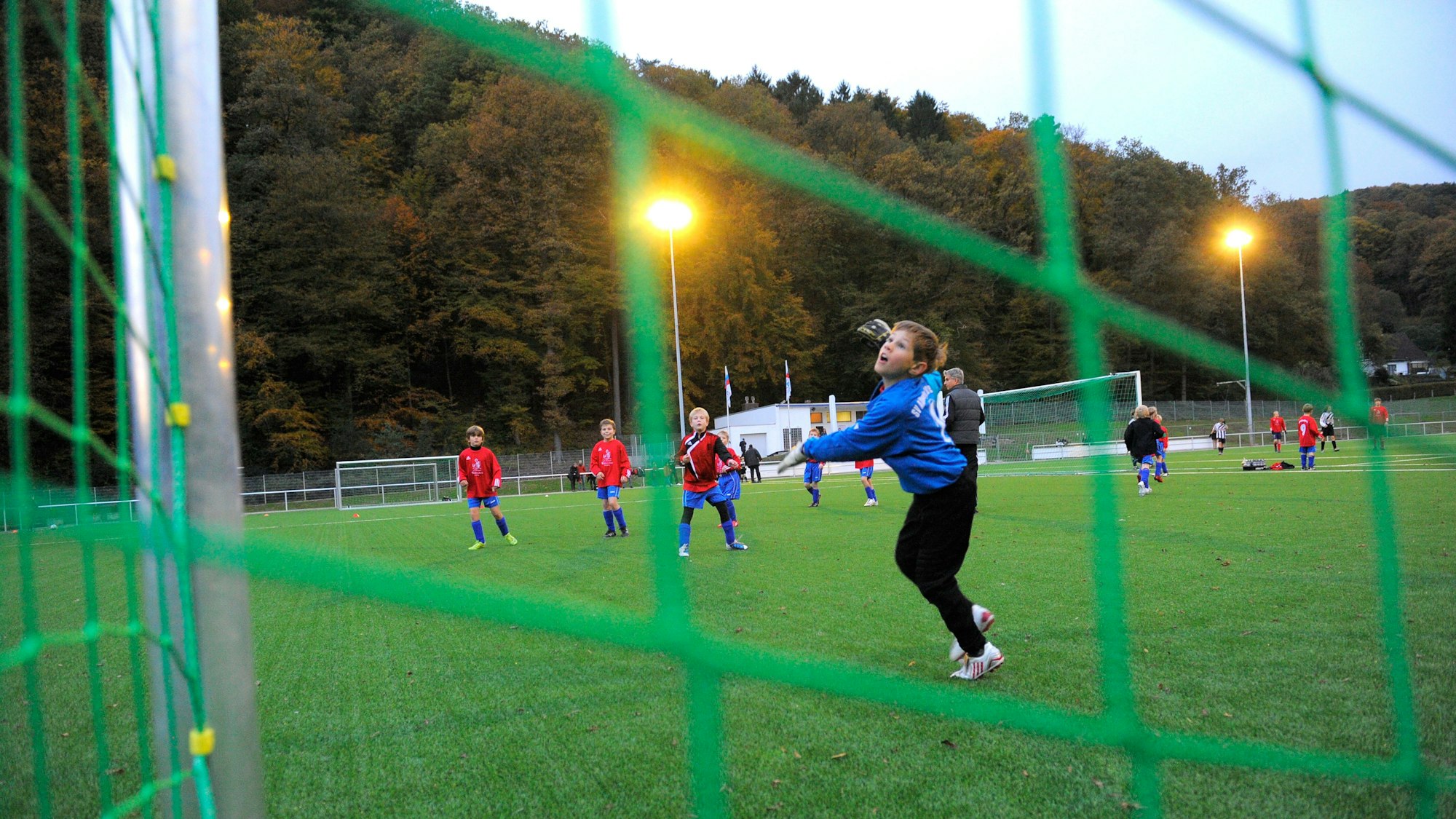 Blick durch das grüne Netz eines Fußballtores auf einen Jungen, der gerade einem Ball hinterherschaut.