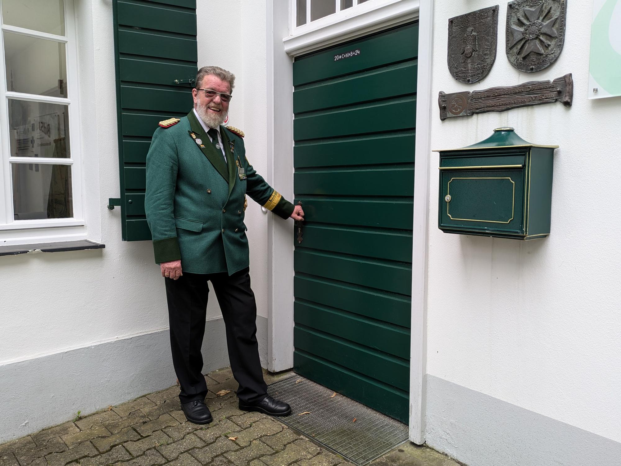 Ein Mann in Uniform steht an einer grünen Holztür.