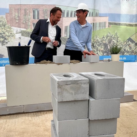 Zwei Männer lachen bei einer Grundsteinlegung.