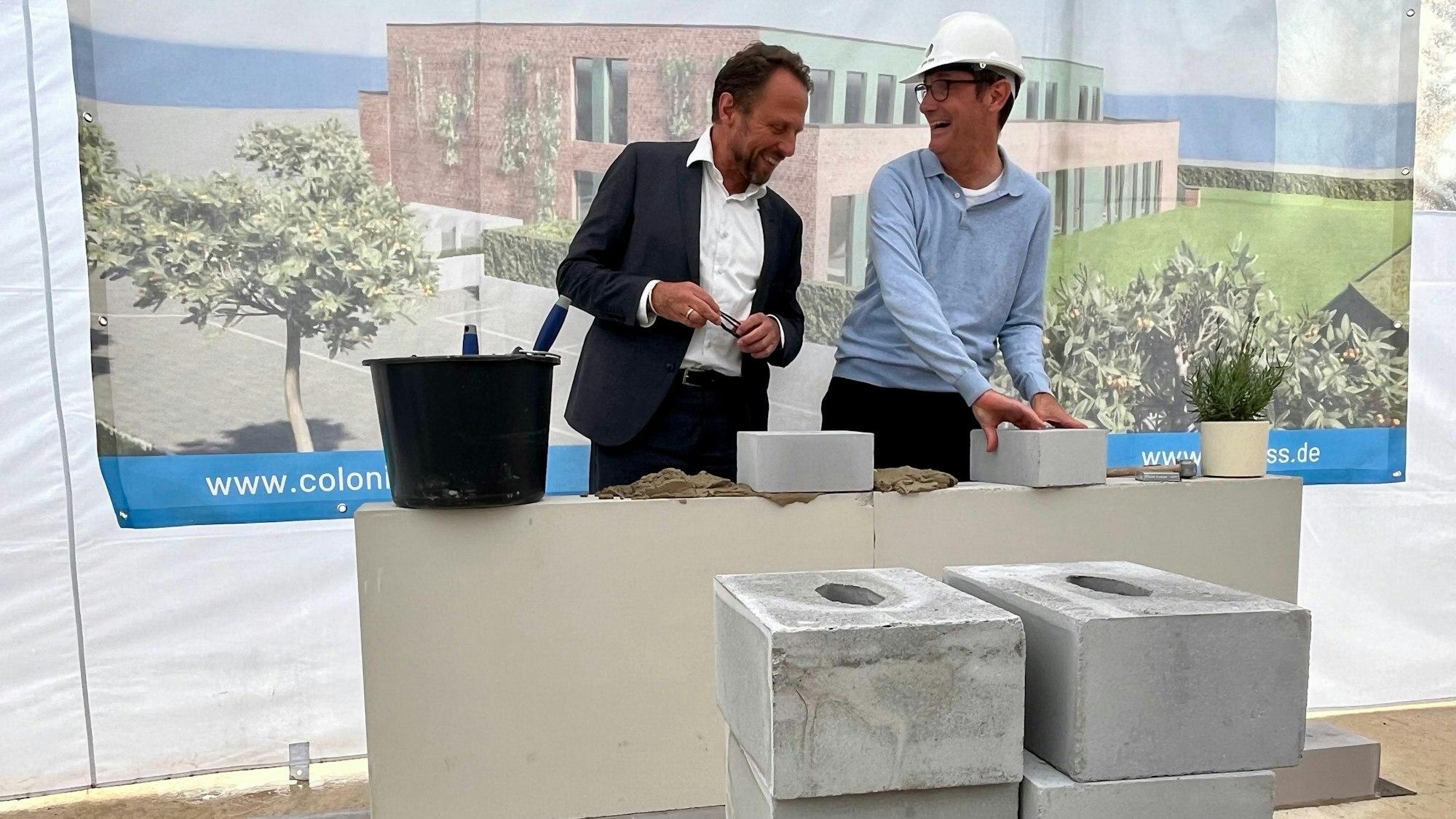Zwei Männer lachen bei einer Grundsteinlegung.