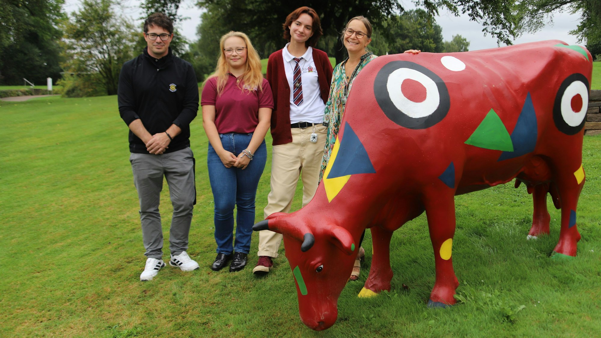 Ein Mann und frei Frauen neben einer bunt bemalten Kuh-Figur