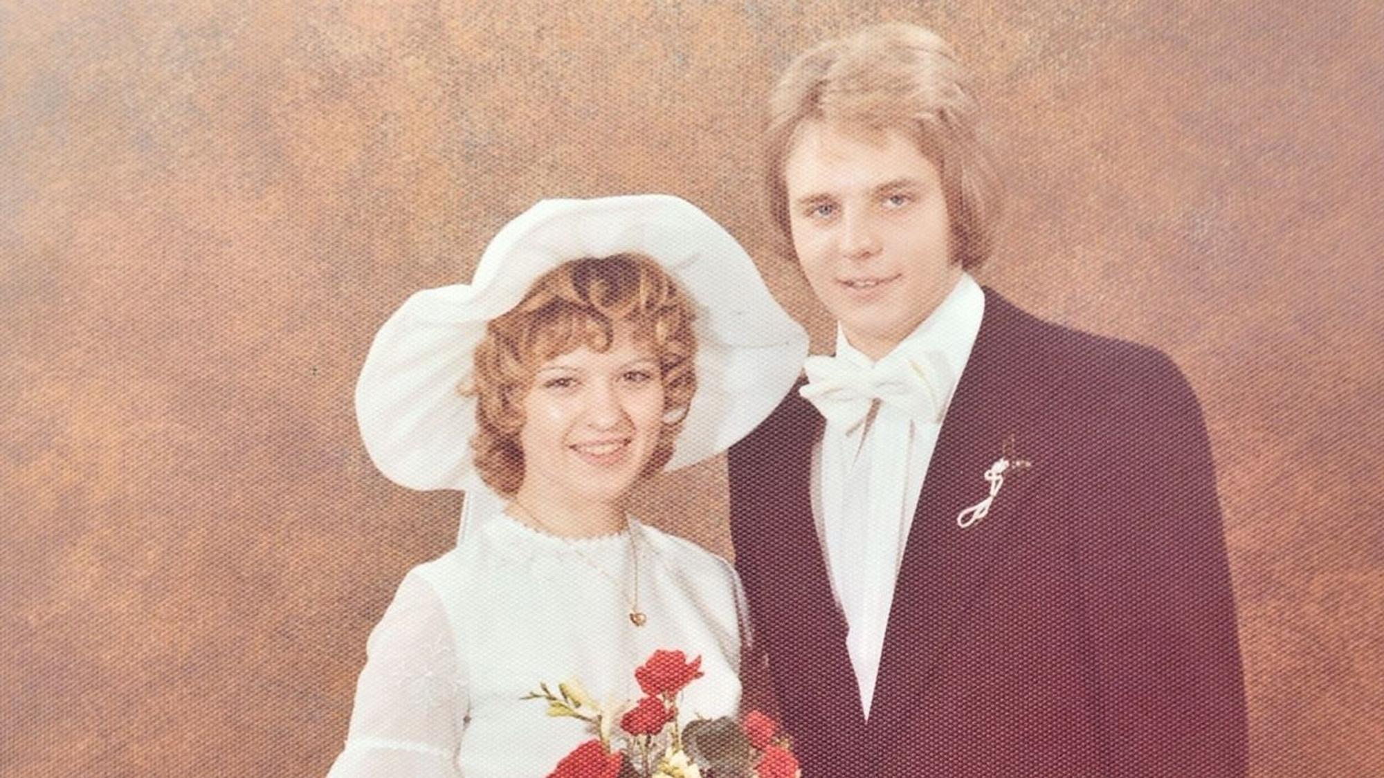 Eine junge Frau und ein junger Mann tragen auf einem Foto aus den 1970er Jahren Kleid und Anzug.