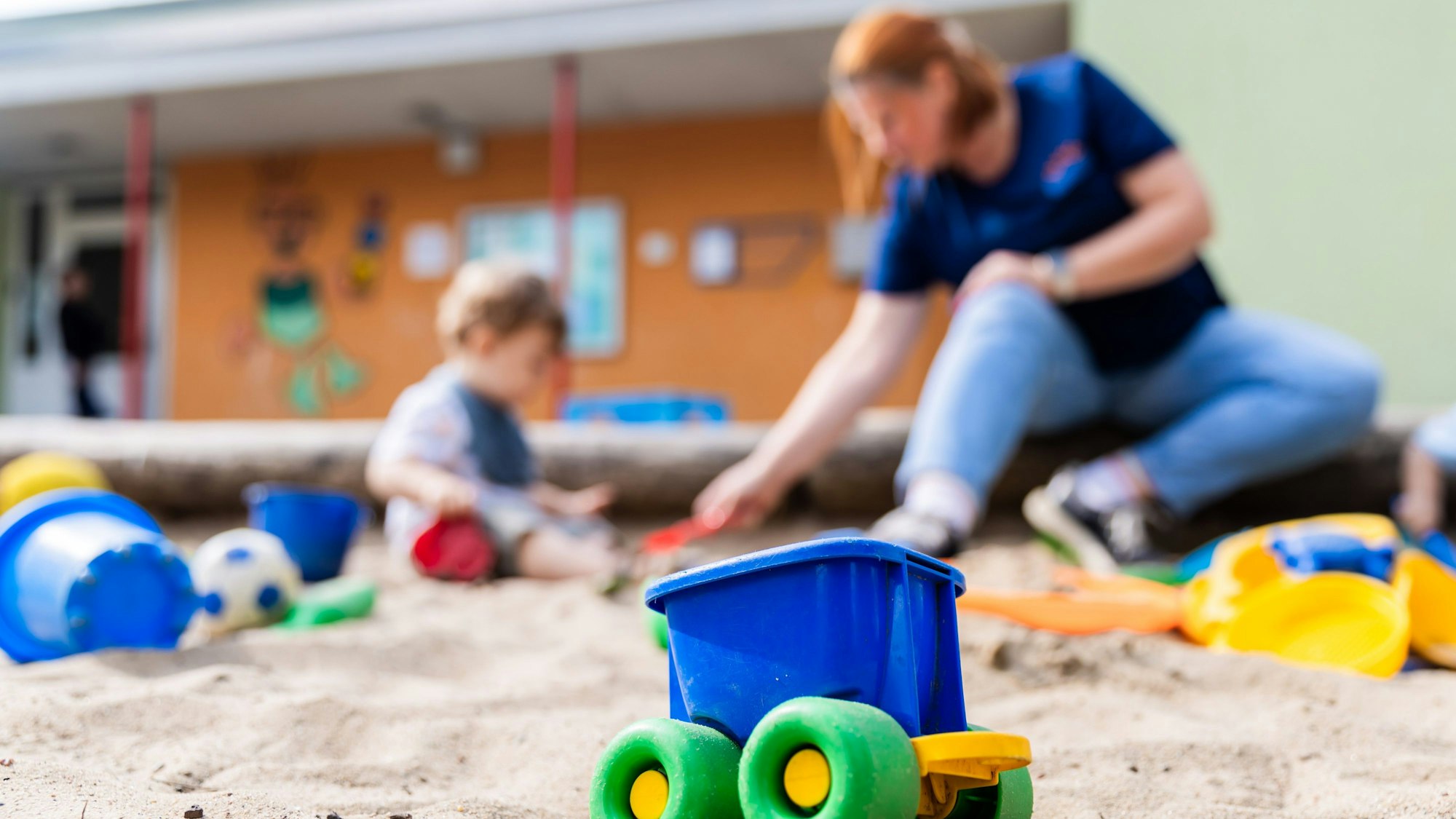Ein Kind spielt mit einer Erzieherin im Sandkasten einer Kita.