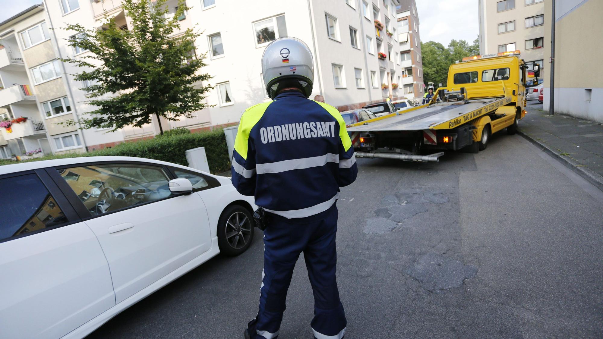 Das Foto zeigt eine Person mit der Aufschrift „Ordnungsamt“ auf der Jacke vor einem Abschleppwagen.