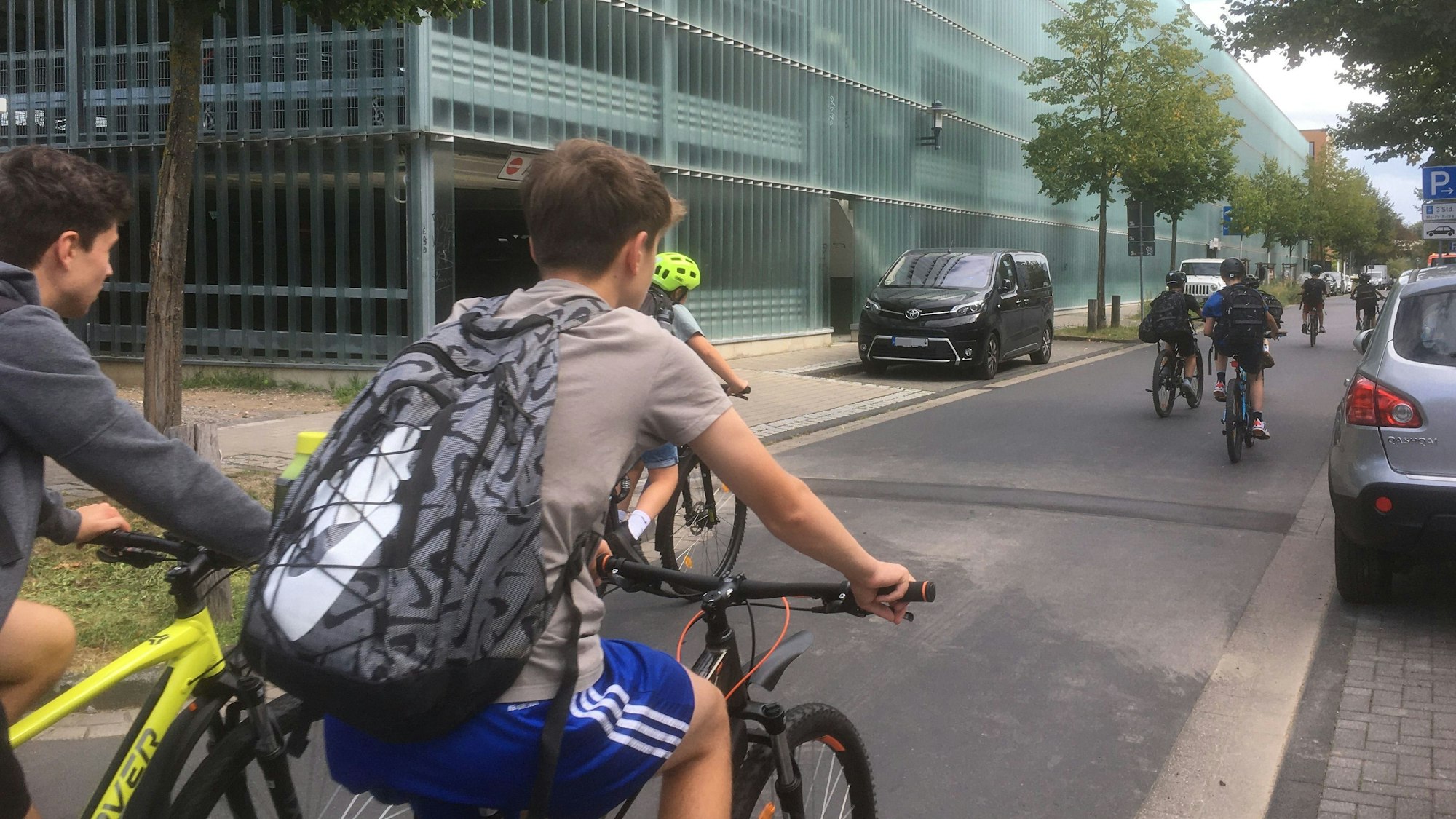 Schüler fahren mit Fahrrädern an einem Parkhaus vorbei.