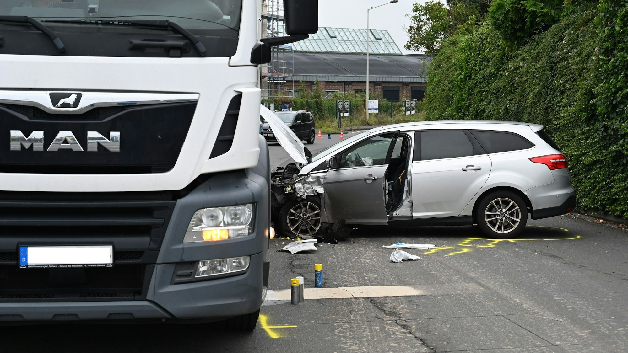 Ein Pkw steht senkrecht neben einem Lkw, die Motorhaube verbeult und kaputt. Auf der Straße sind in Neon-Gelb Markierungen der Polizei angebracht.
