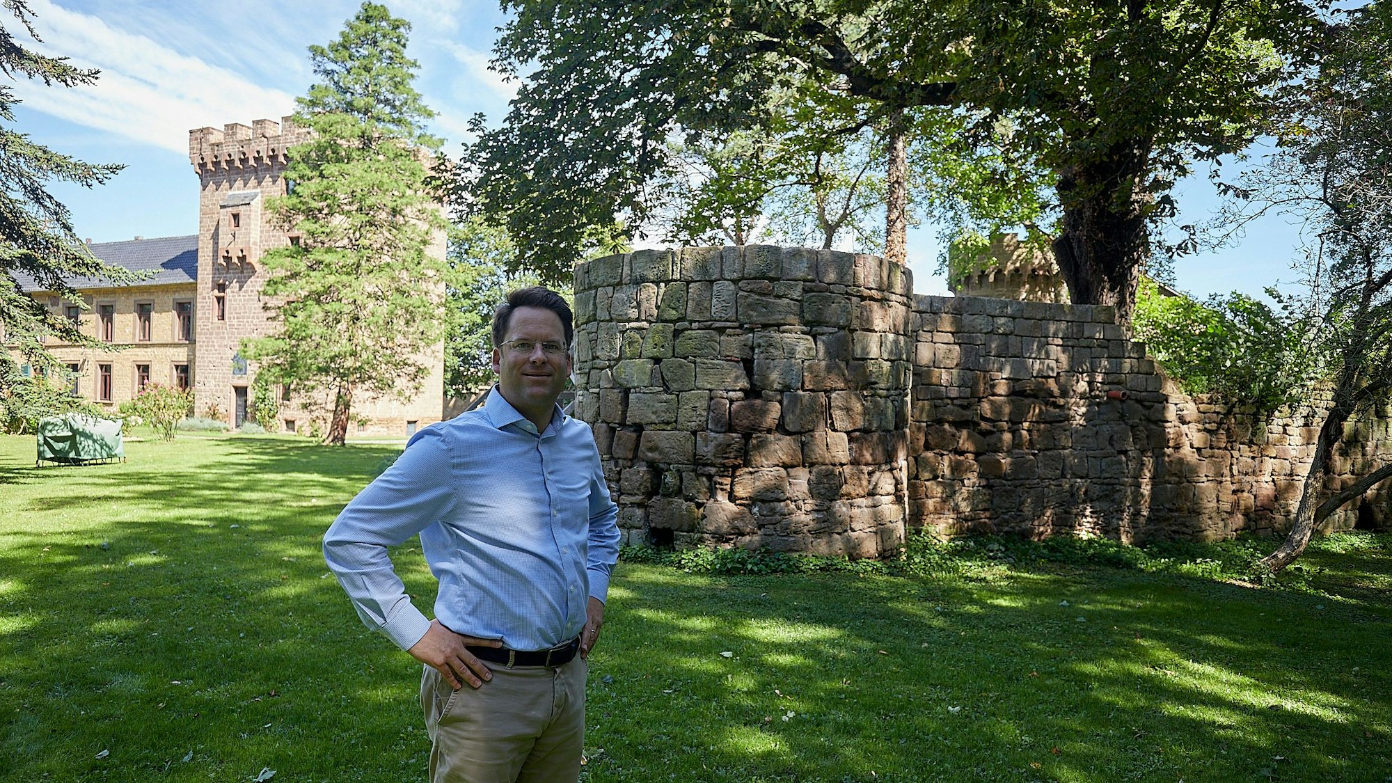 Oliver von Gagern steht auf einer Rasenfläche, die Burg hinter ihm wird von Bäumen flankiert.