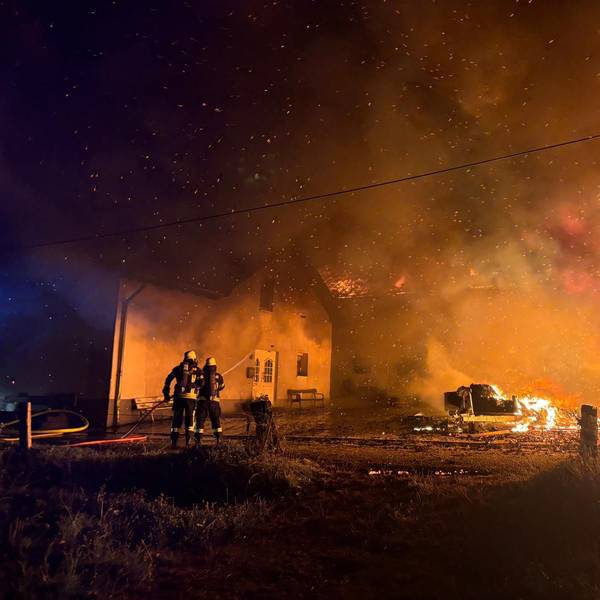 Feuerwehrleute löschen Flammen und bewässern ein Wohngebäude, damit dieses nicht Feuer fängt.