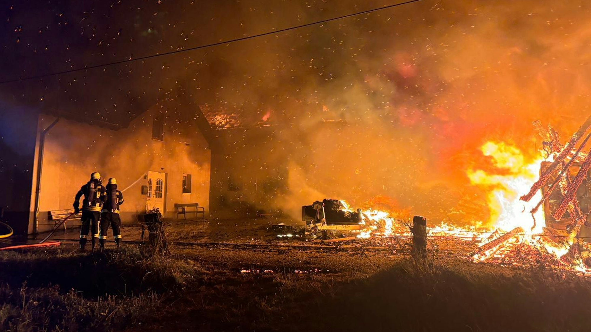 Feuerwehrleute löschen Flammen und bewässern ein Wohngebäude, damit dieses nicht Feuer fängt.